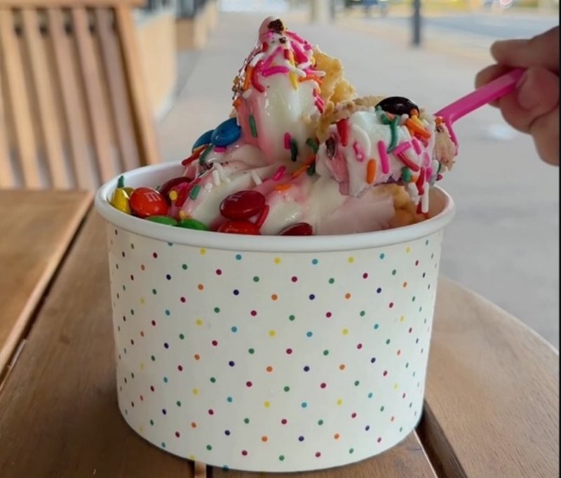 A loaded cup of frozen yogurt with fruit, candy, and sauce toppings